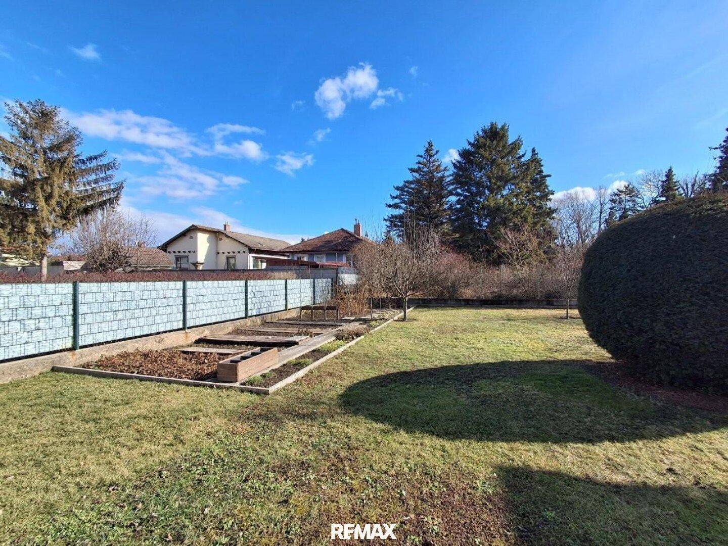 Großer Garten mit Rasenfläche, Hochbeeten und umgebenden Bäumen.