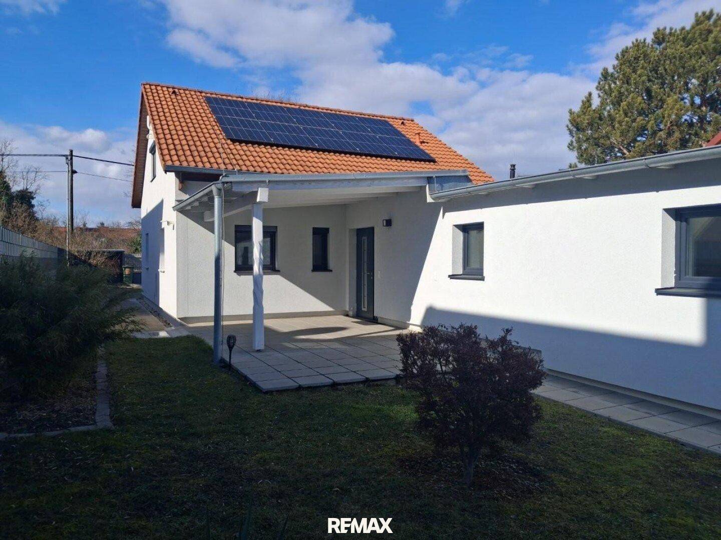 Rückansicht des Hauses mit Rasenfläche, Terrasse und Solaranlage auf dem Dach.