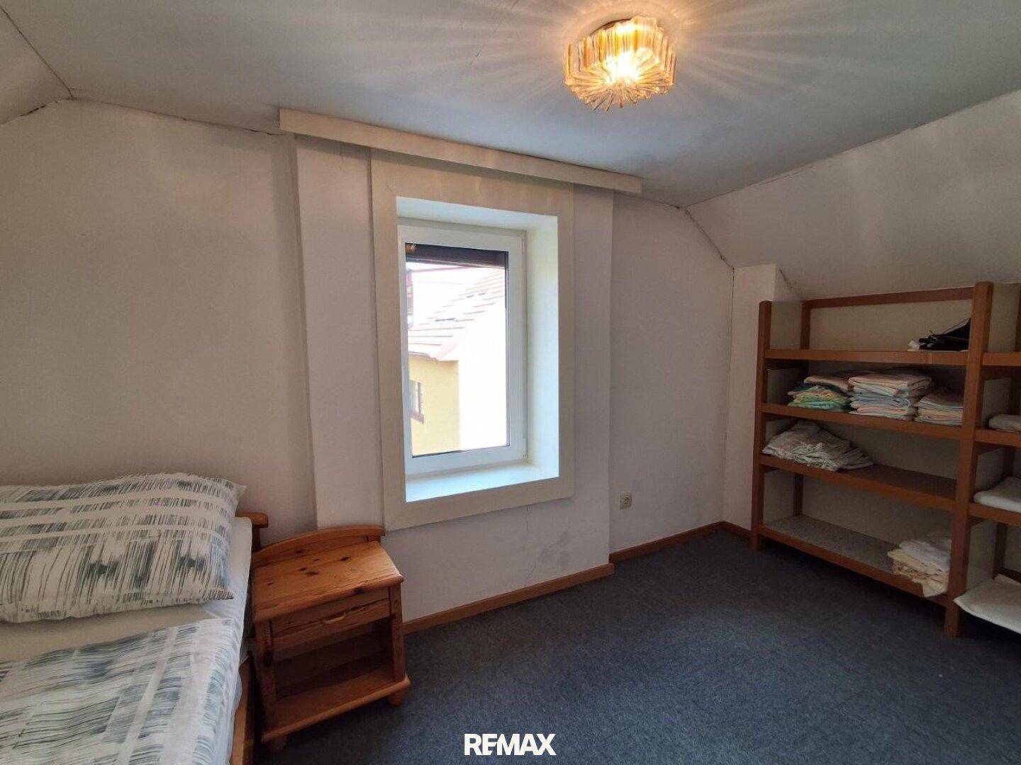 Helles Schlafzimmer im Dachgeschoss mit Teppichboden, Fenster und Holzregal.