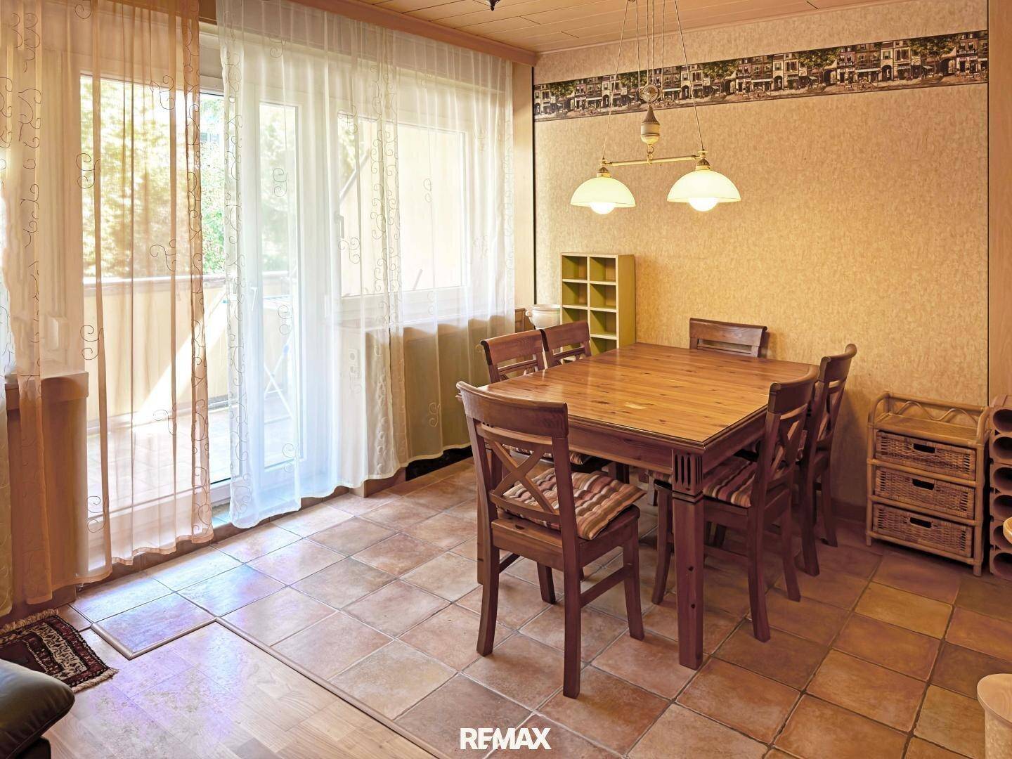 Essbereich mit Holztisch und Stühlen, Fliesenboden und Zugang zu einem Balkon oder Terrasse.