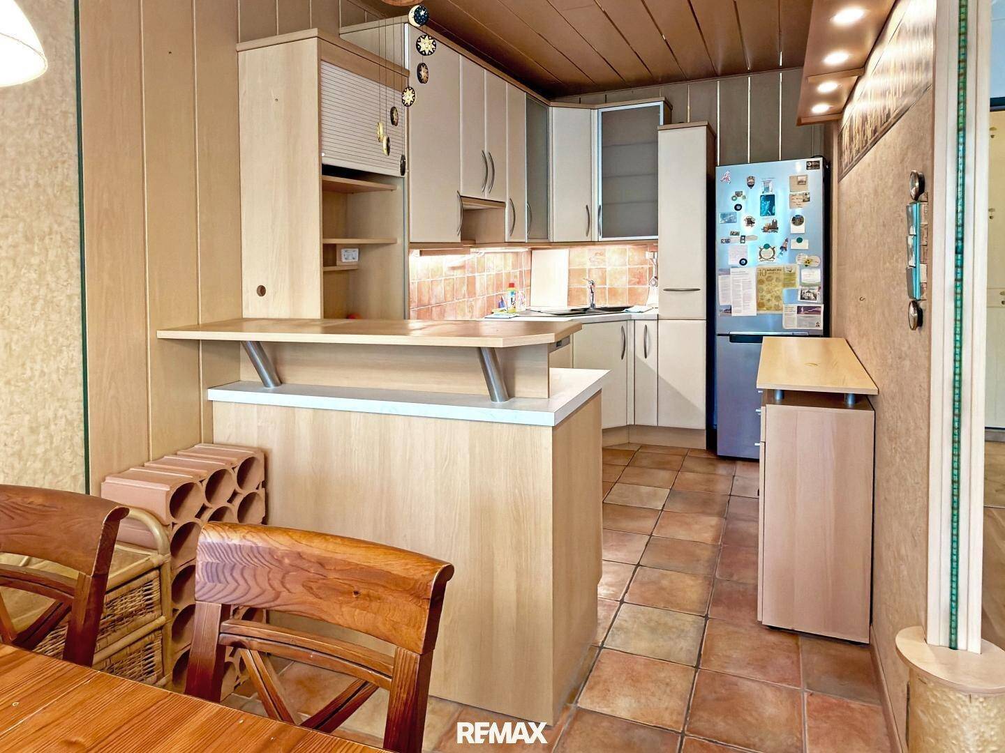 Küche mit Holzschränken, Frühstücksbar und Kühlschrank, verbunden mit dem Essbereich.