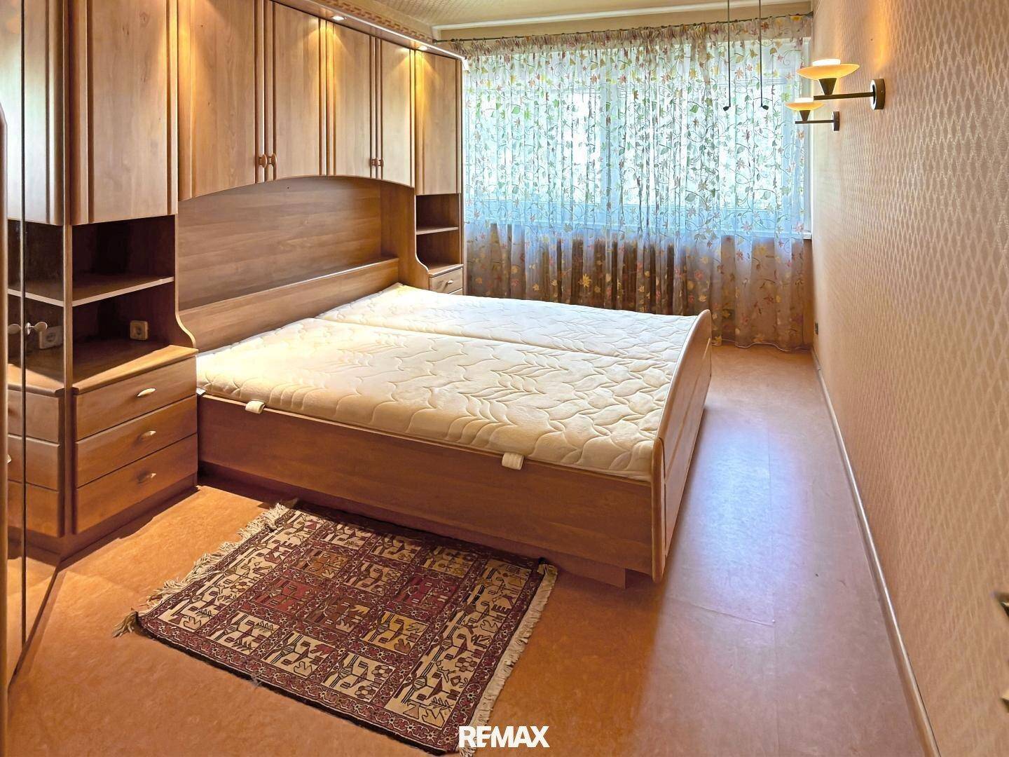 Schlafzimmer mit großem Doppelbett, integrierten Holzschränken und gemusterter Tapete.