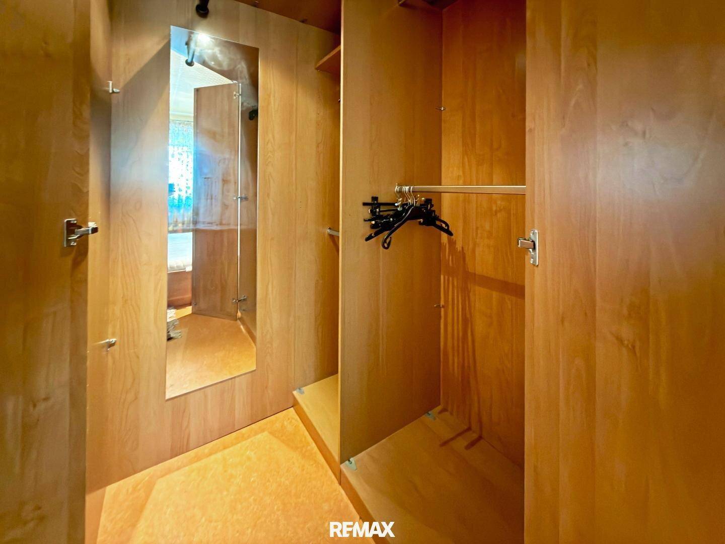 Begehbarer Kleiderschrank mit Holzregalen, Kleiderstange und großem Spiegel an der Tür.