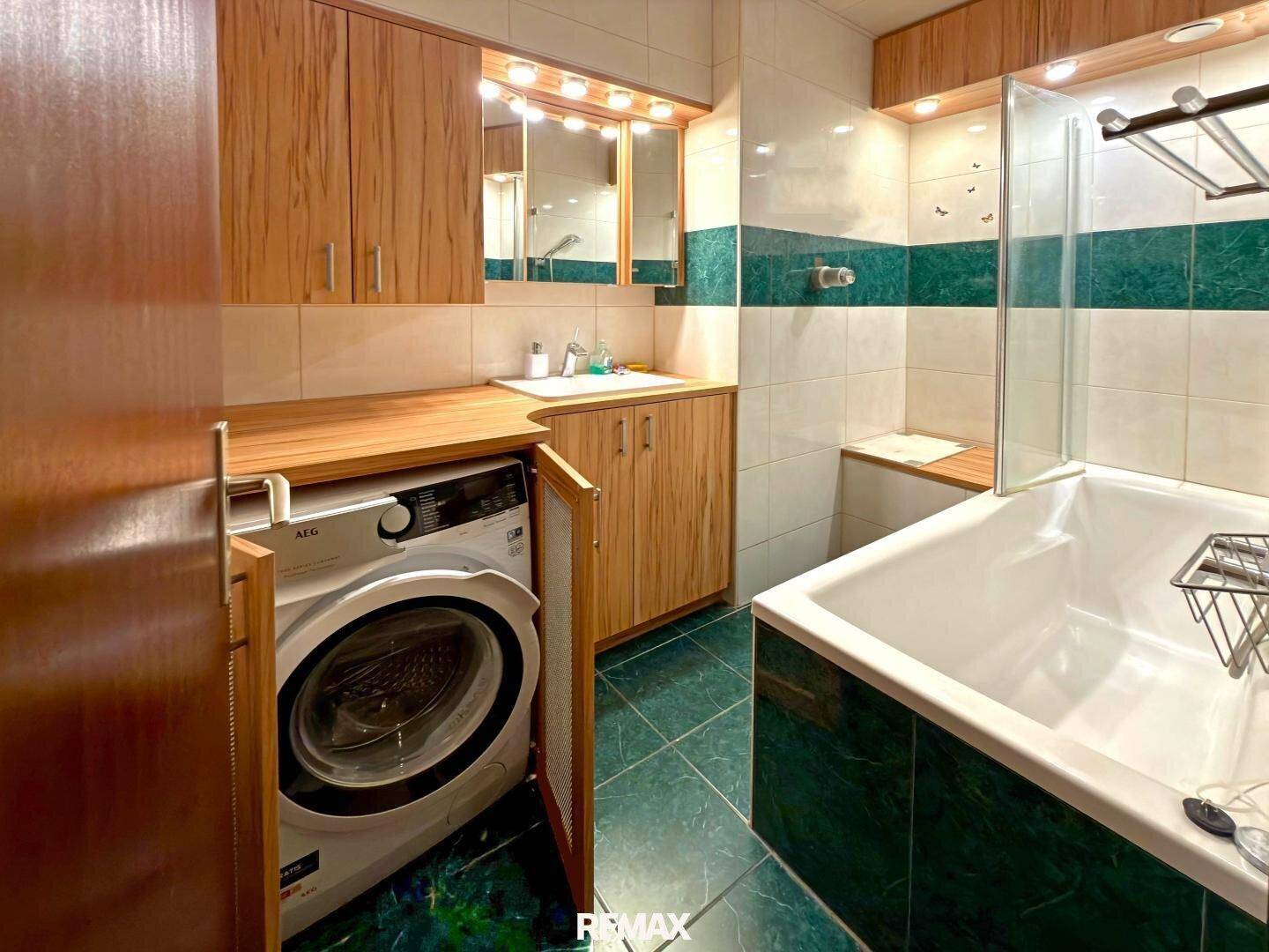 Badezimmer mit Badewanne, Waschbecken, Holzschränken und integrierter Waschmaschine.