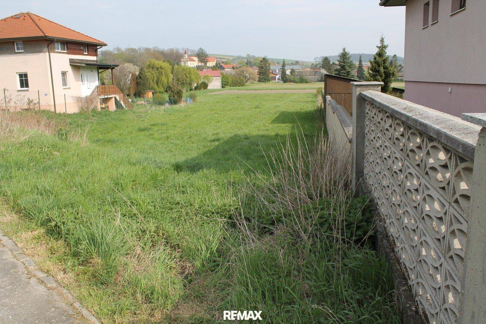 Grünes Grundstück mit angrenzendem Haus und dekorativem Zaun, umgeben von ländlicher Bebauung.