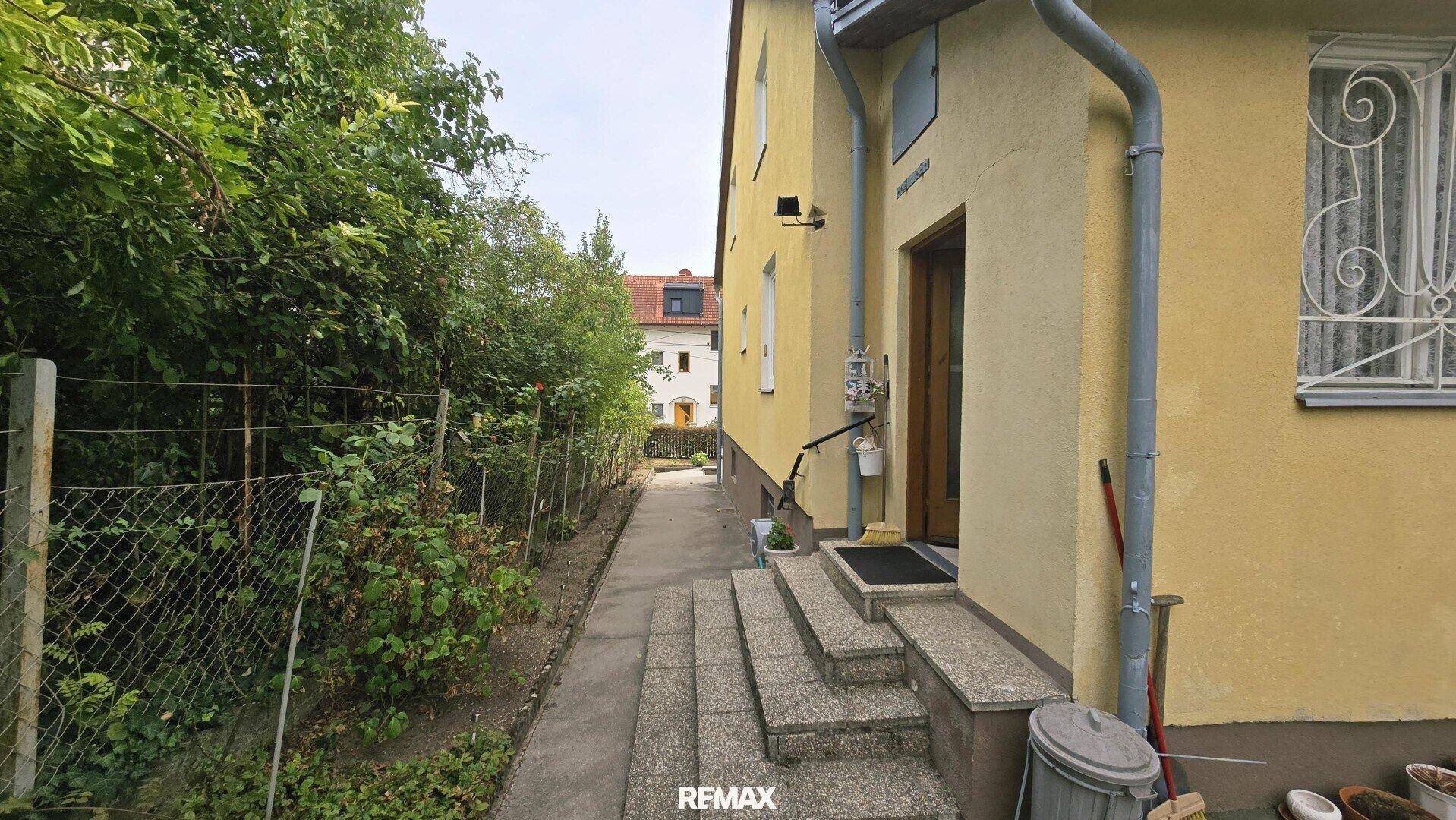 Seitlicher Zugang zum Haus mit Steinstufen und einem Zaun entlang des Grundstücks.