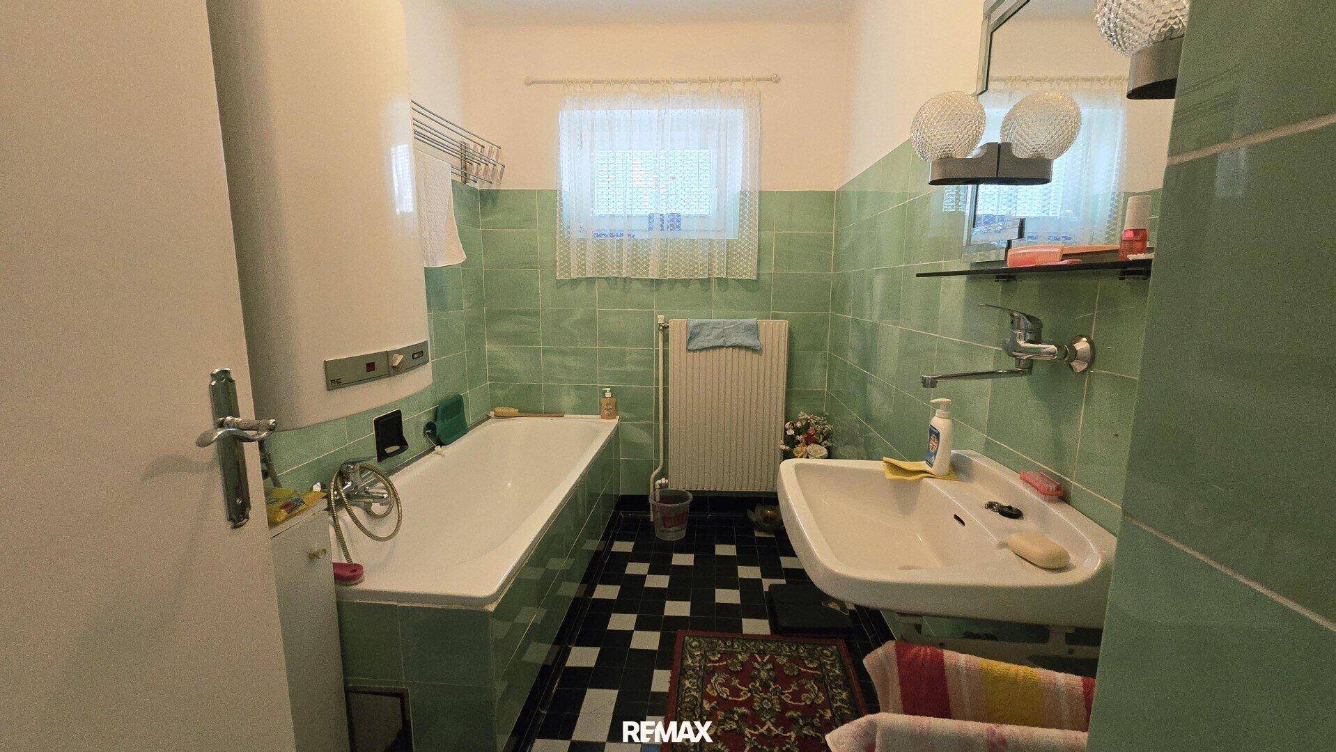 Badezimmer im Stil der 80er Jahre mit grünen Fliesen, Badewanne und Waschbecken.