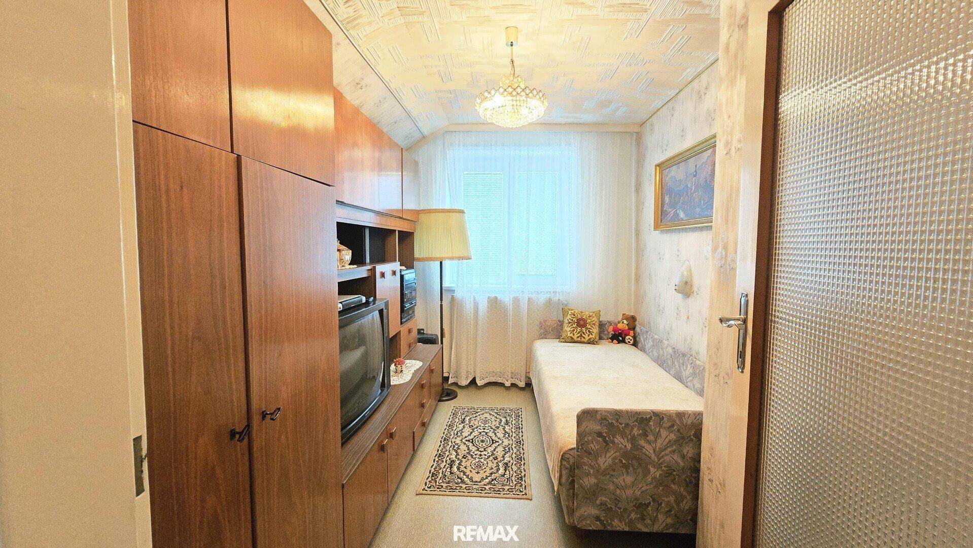Kleines Schlafzimmer mit Einzelbett, Holzschrank und Fenster.
