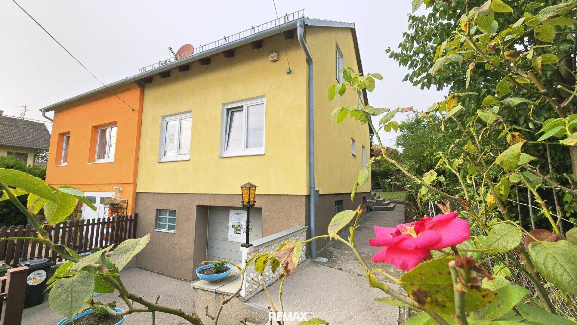 Seitenansicht des gelben Hauses mit Eingangsbereich und einer blühenden Rose im Vordergrund.