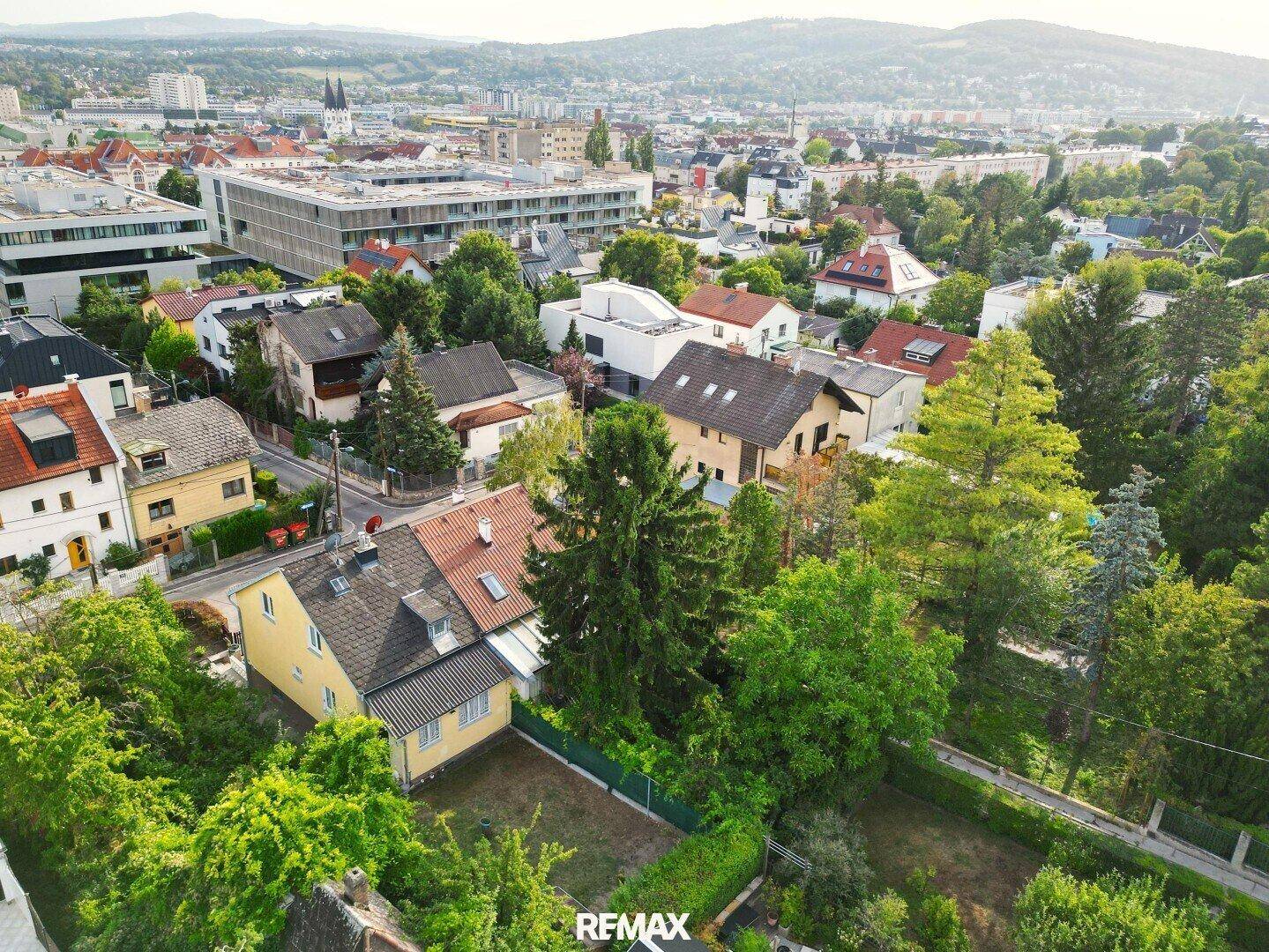 Weitläufige Luftaufnahme der Wohngegend mit vielen Grünflächen und städtischer Skyline im Hintergrund.