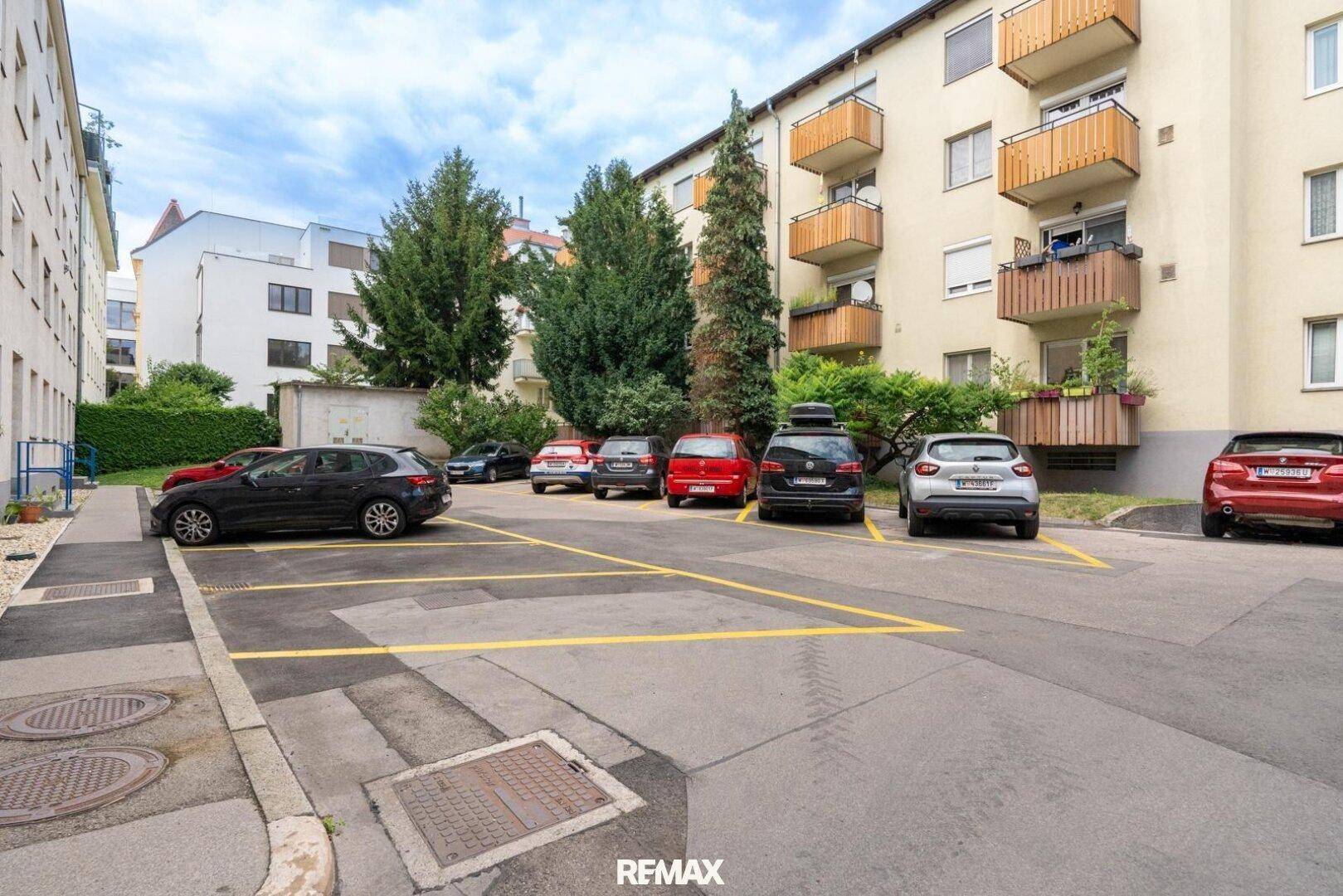 Außenparkplätze auf einem Hof mit umliegenden Wohngebäuden und Bäumen.