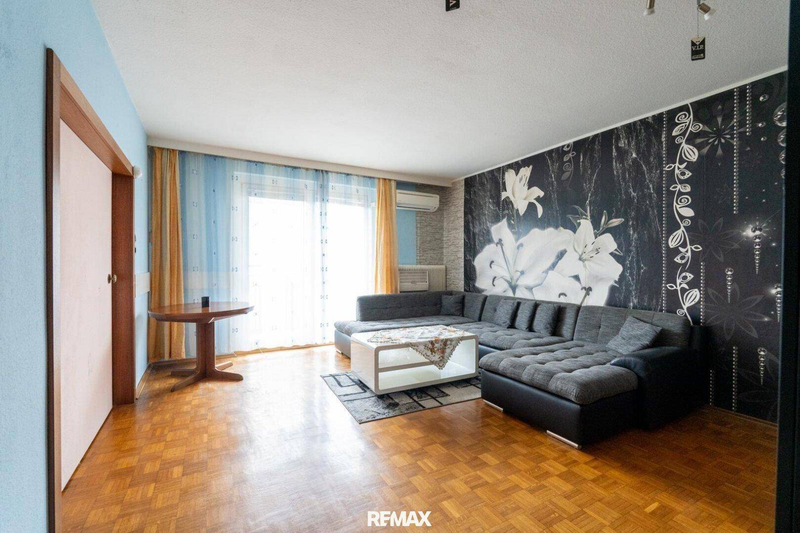 Geräumiges Wohnzimmer mit Parkettboden, Ecksofa und Zugang zu einem Balkon.