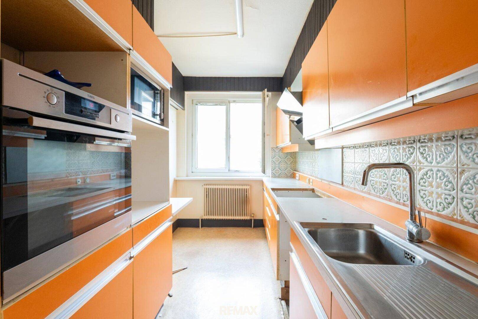 Küche im Retro-Stil mit orangefarbenen Schränken, Fliesen und Einbaugeräten.