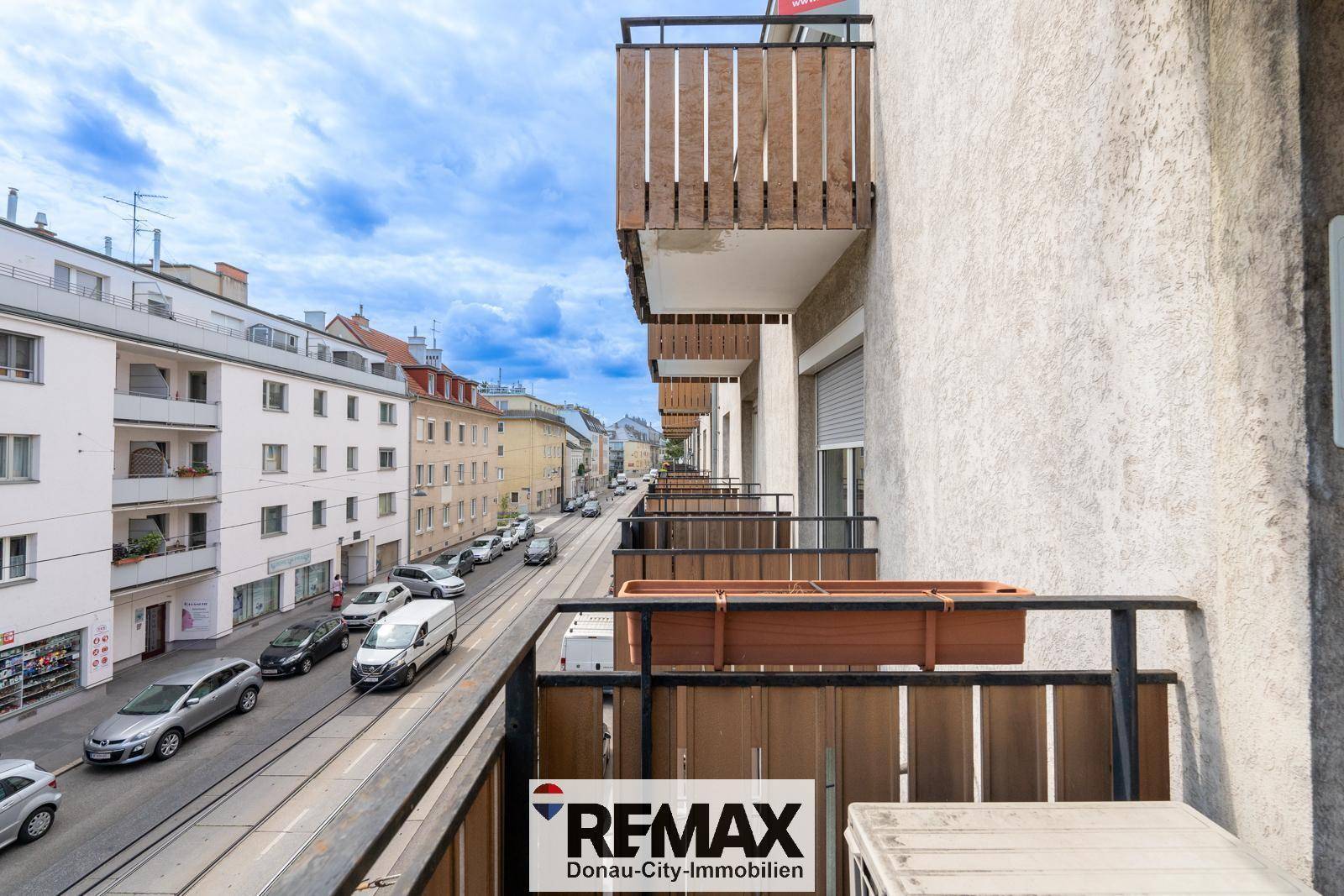Balkon mit Holzbalkonbrüstung und Blick auf die belebte Stadtstraße mit parkenden Autos.