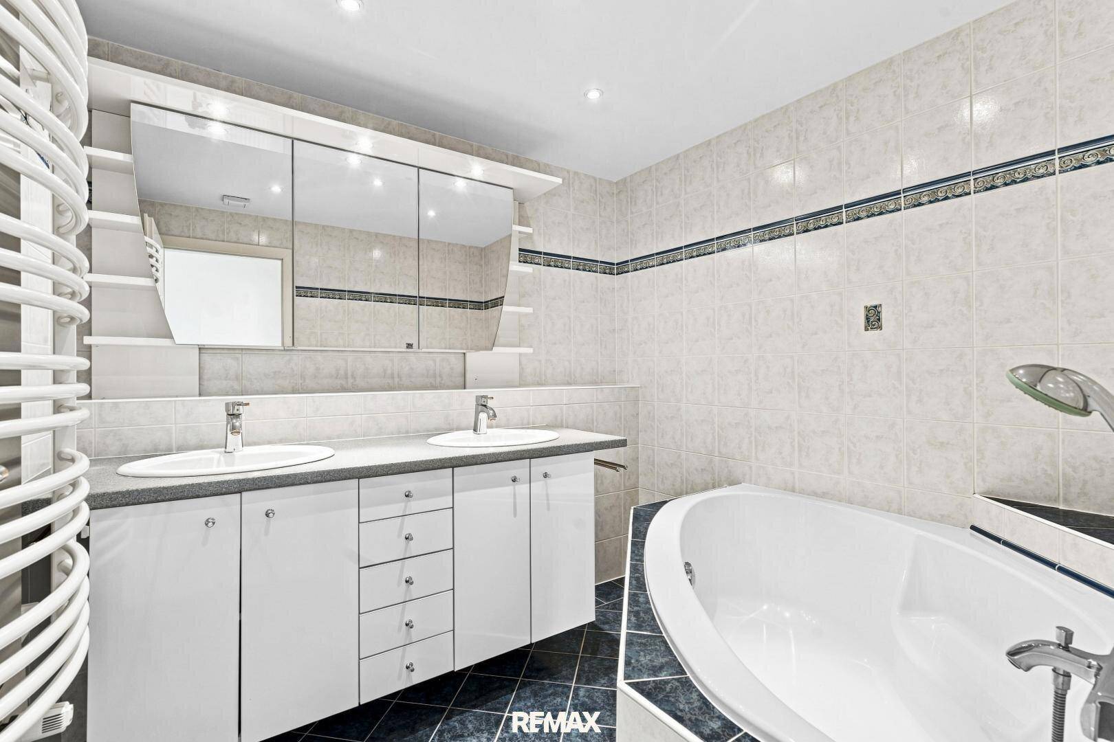 Modernes Badezimmer mit Doppelwaschbecken, Badewanne und weißen Fliesen.