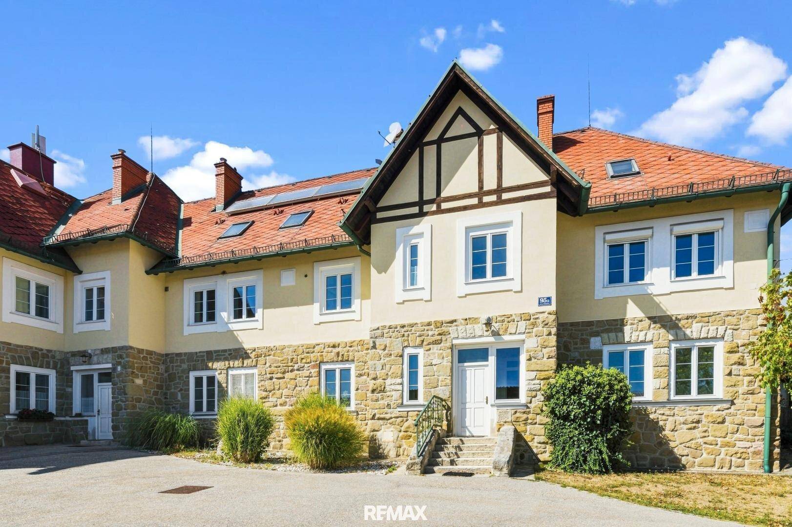 Traditionelles Gebäude mit Steinfassade, weißen Fenstern und einem roten Ziegeldach.