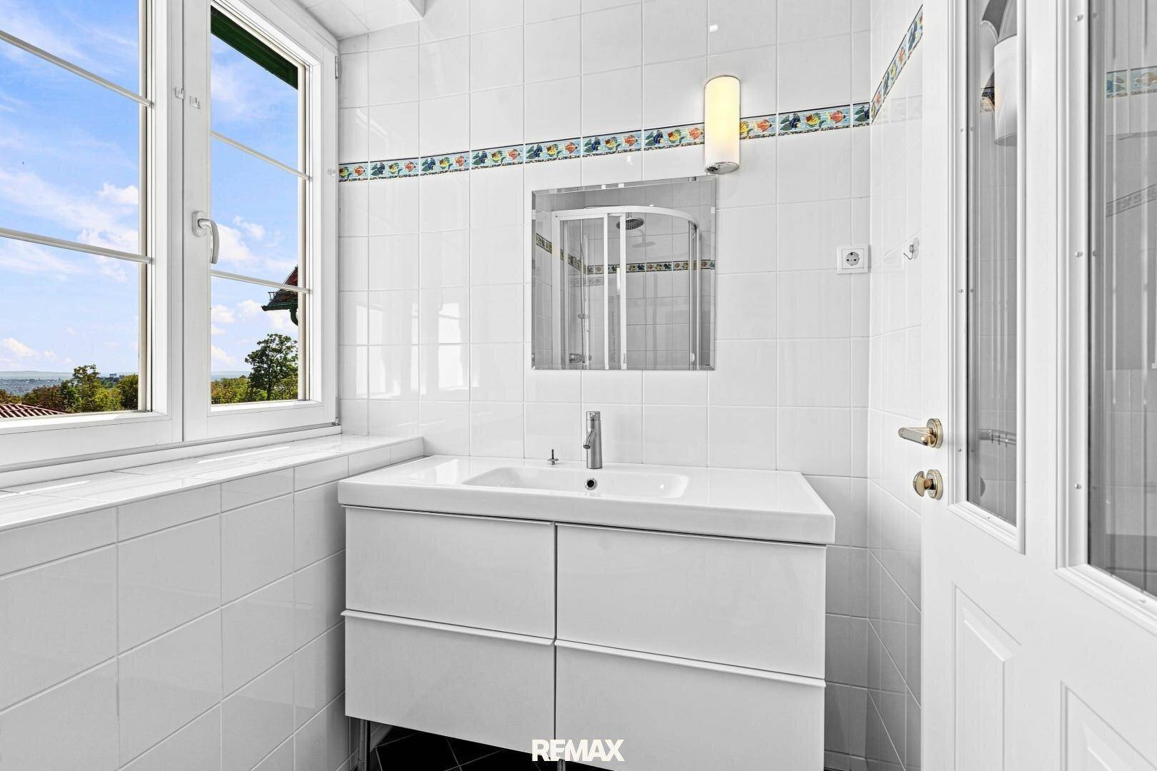 Helles Badezimmer mit weißem Waschbecken, Spiegelschrank und Fenster mit Ausblick.