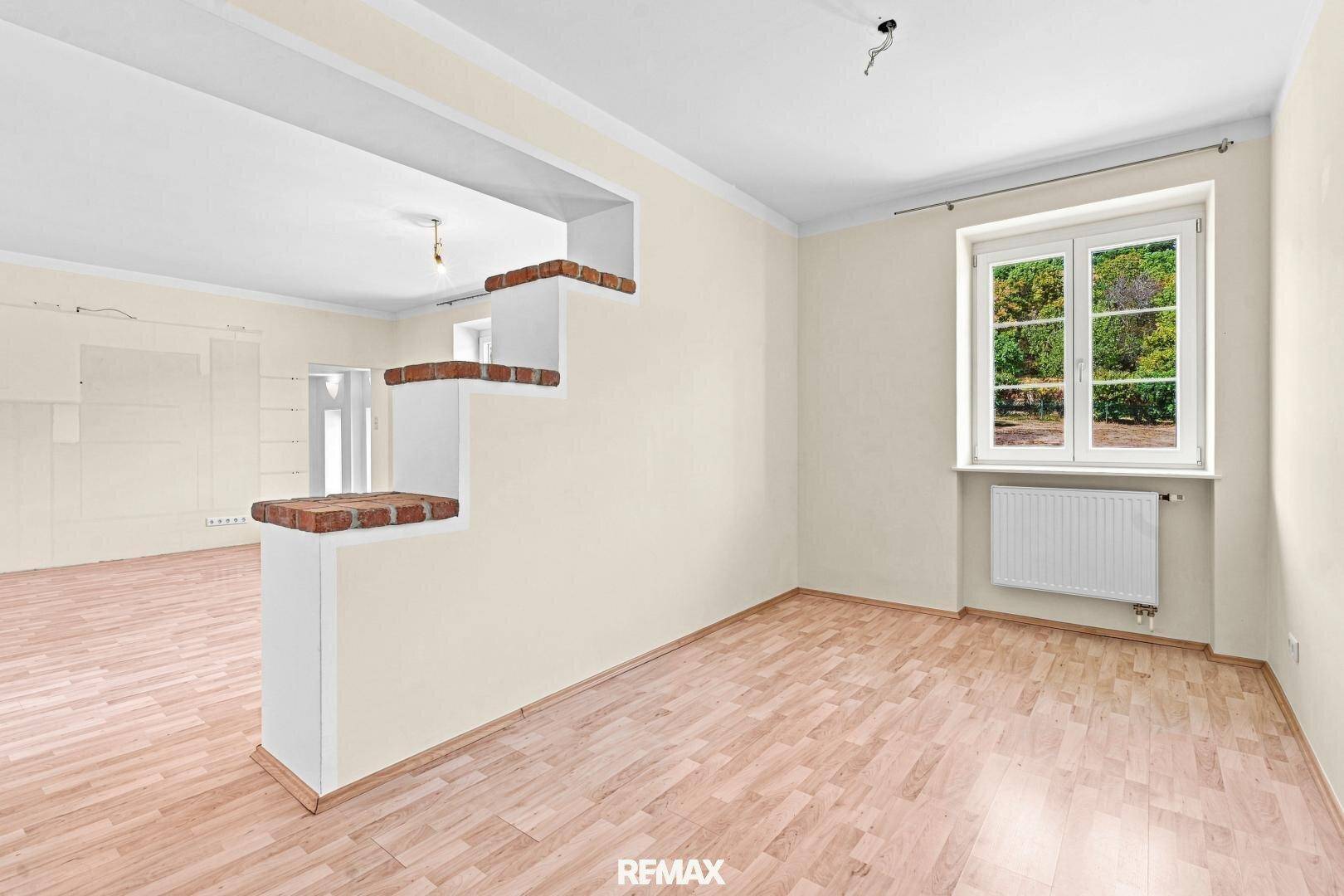 Geräumiges Wohnzimmer mit Parkettboden und einem dekorativen Mauerelement, das den Raum teilt.