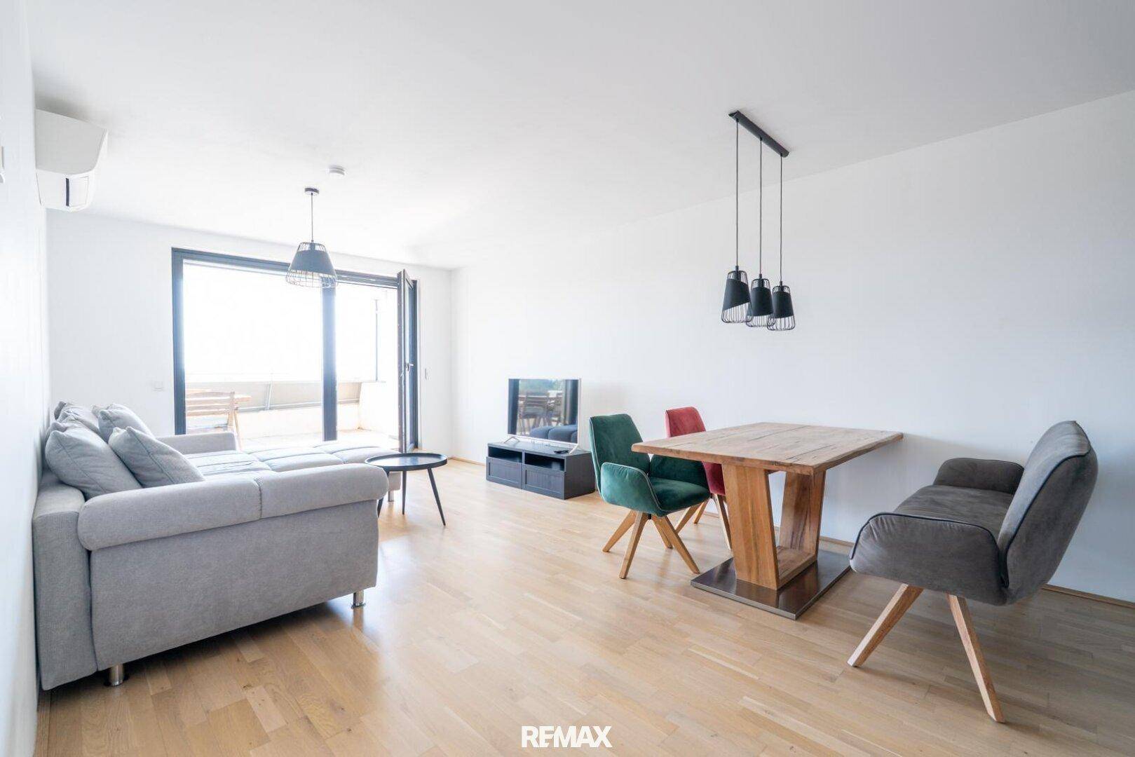 Heller Wohn- und Essbereich mit Holzboden, Klimaanlage und Zugang zum Balkon.