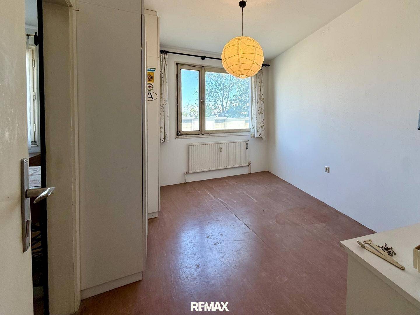 Heller Raum mit Fenster, Heizkörper und einfacher Bodengestaltung.