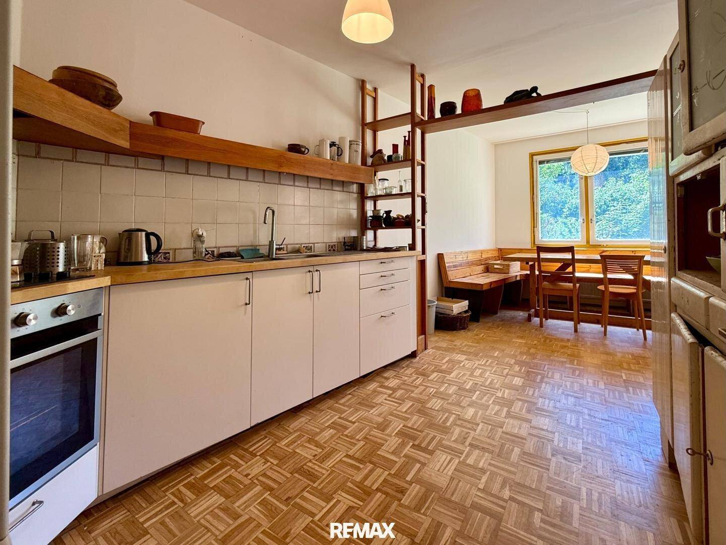 Offene Küche mit Essbereich, Holzmöbeln und Blick ins Grüne durch das Fenster.