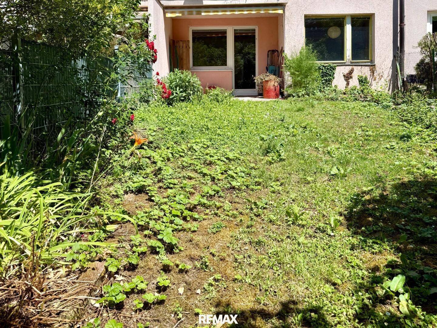 Garten mit Terrasse und Zugang zum Gebäude, umgeben von viel Grün.