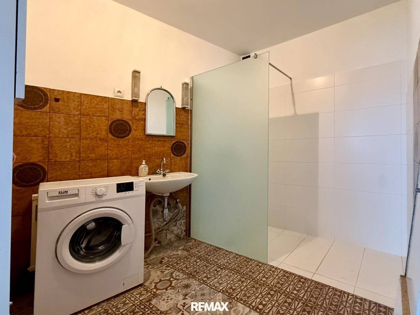 Badezimmer mit Dusche, Waschbecken, Spiegel und Waschmaschine.
