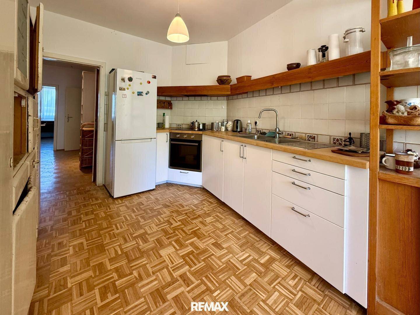 Funktionale Küche mit weißen Unterschränken, Holzregalen und Parkettboden.