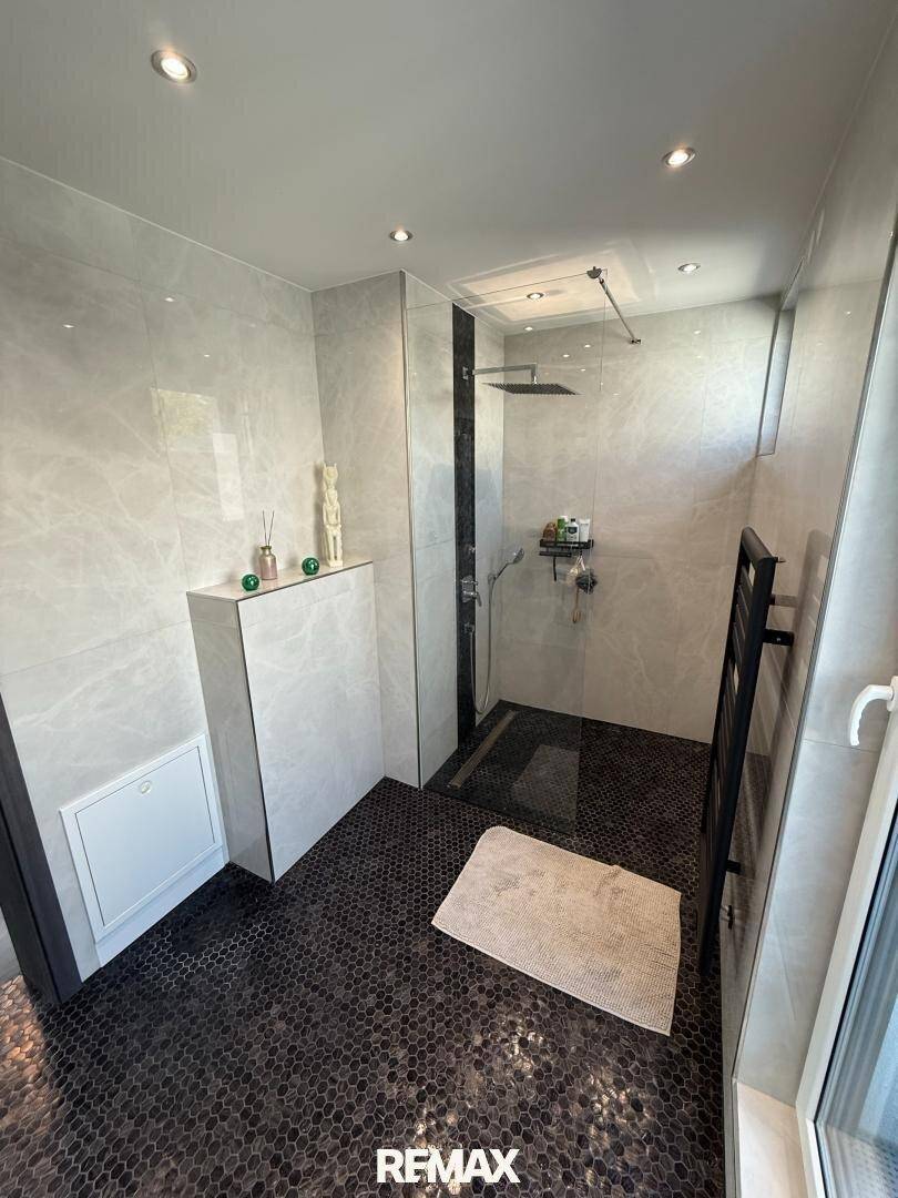 Helles Badezimmer mit begehbarer Dusche, dunklem Mosaikboden und beheiztem Handtuchhalter.