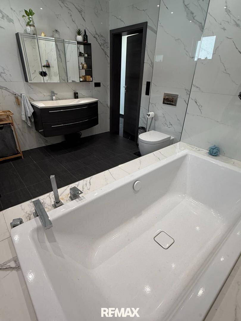 Elegantes Badezimmer mit großer Badewanne, Marmorfliesen und modernem Waschtisch.