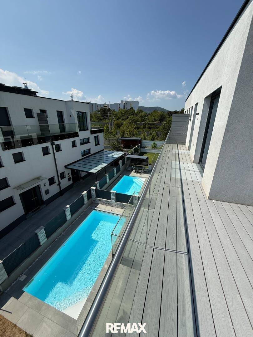 Weitläufige Dachterrasse mit Holzdeck und Blick auf die Pools der Anlage.
