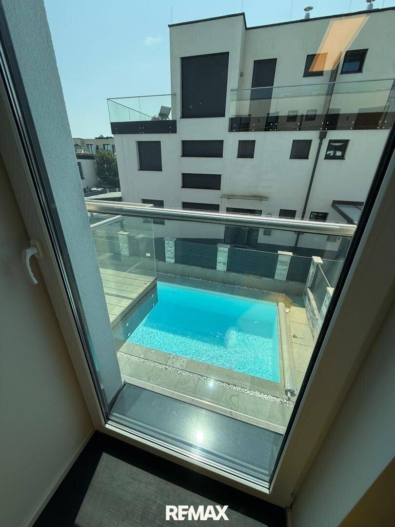 Blick aus dem Fenster auf den privaten Poolbereich und die moderne Architektur des Gebäudes.