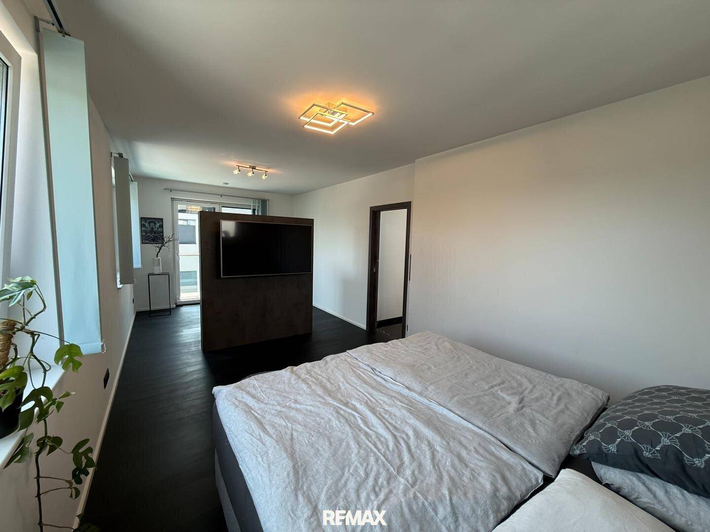 Geräumiges Schlafzimmer mit dunklem Boden, viel Tageslicht und moderner Einrichtung.
