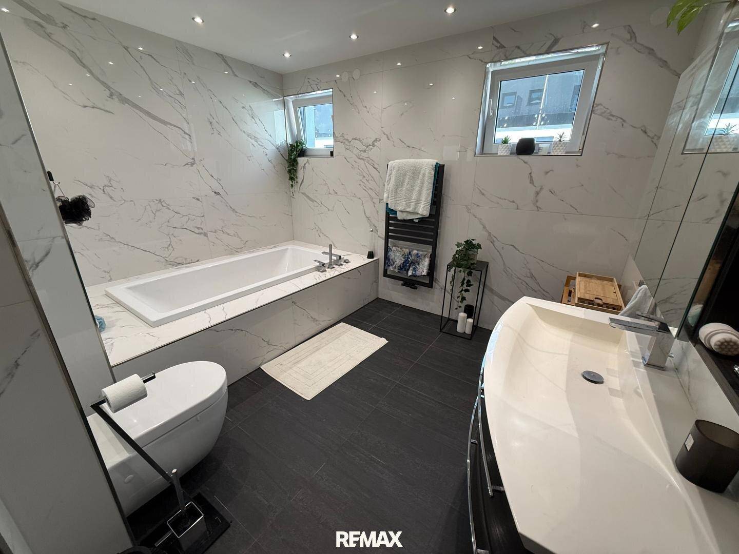 Modernes Badezimmer mit großer Badewanne, Marmorfliesen und beheiztem Handtuchhalter.