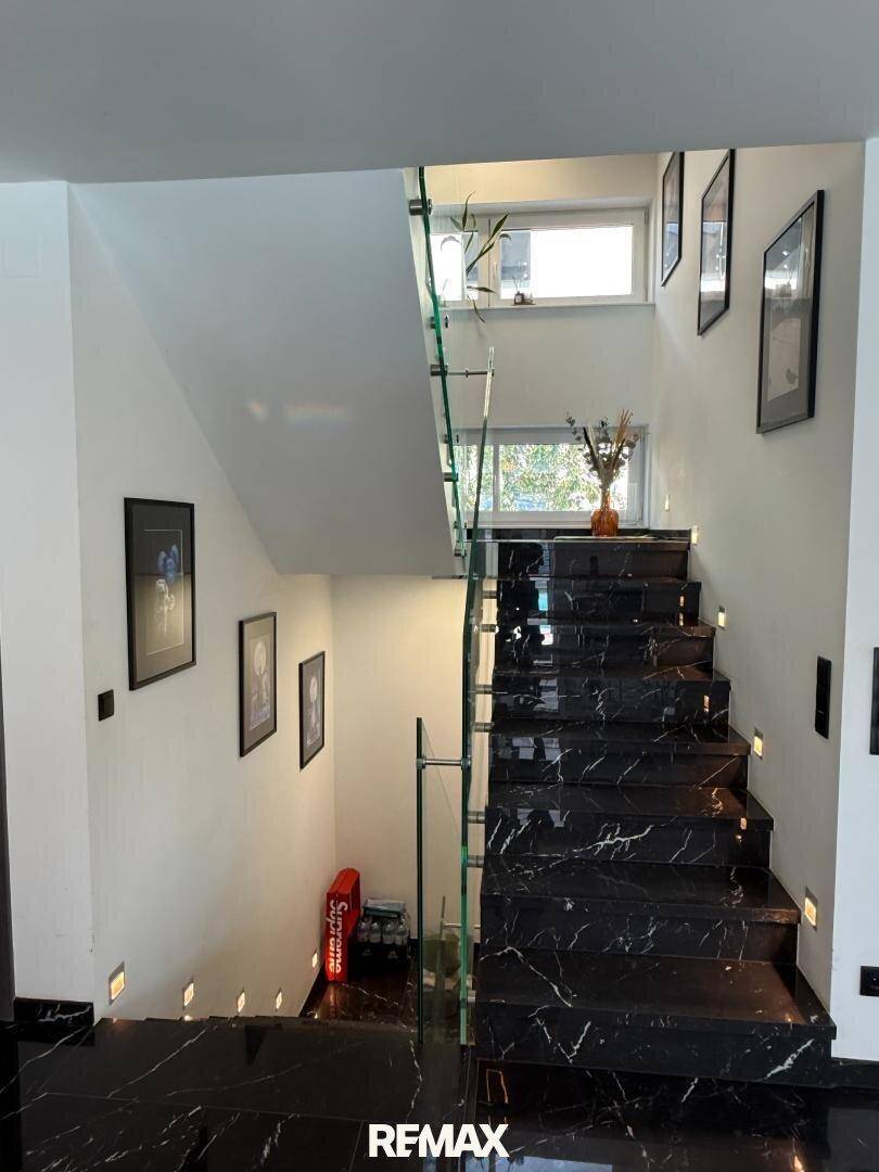 Elegante Treppe mit schwarzem Marmor und Glasgeländer, modern beleuchtet.