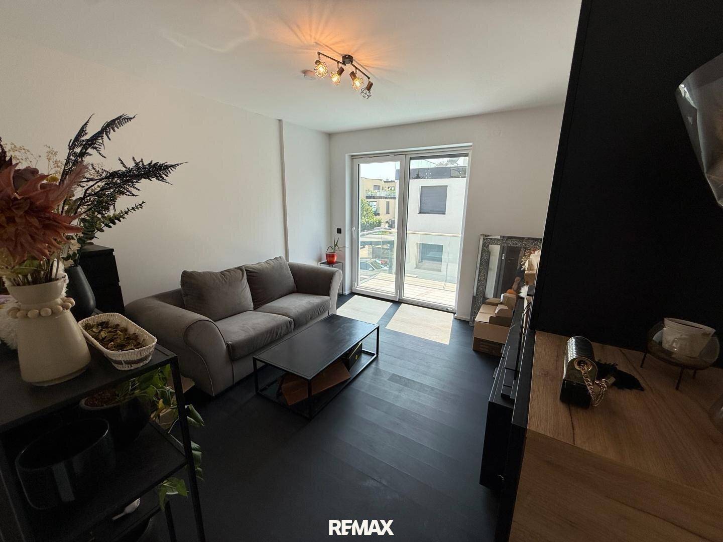 Gemütliches Wohnzimmer mit dunklem Boden, bequemer Couch und Zugang zum Balkon.