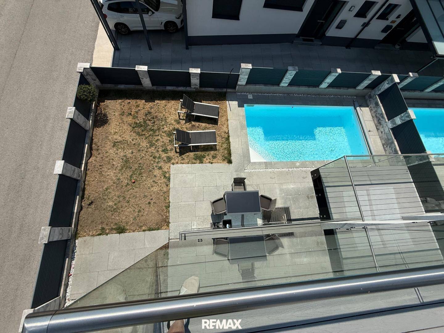 Blick von oben auf den Gartenbereich mit Pool, Liegestühlen und Essbereich.