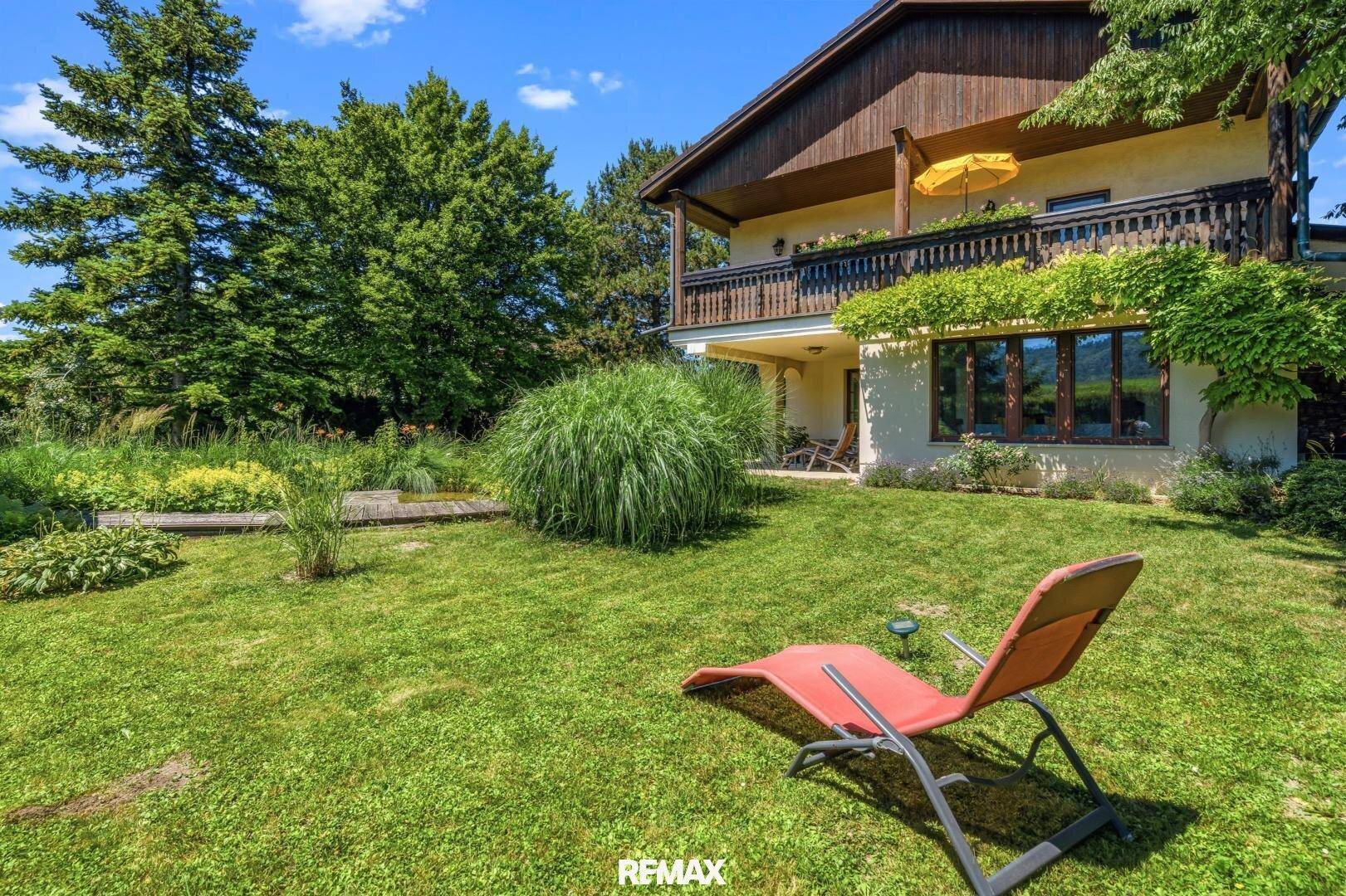 Gepflegter Garten mit Rasenfläche, Liegestuhl und üppiger Bepflanzung.