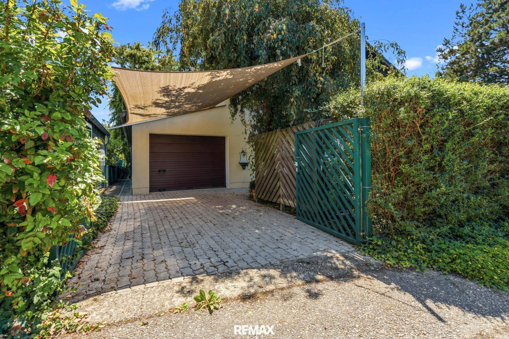 Einfahrt mit Garage, Sonnensegel und grüner Hecke.