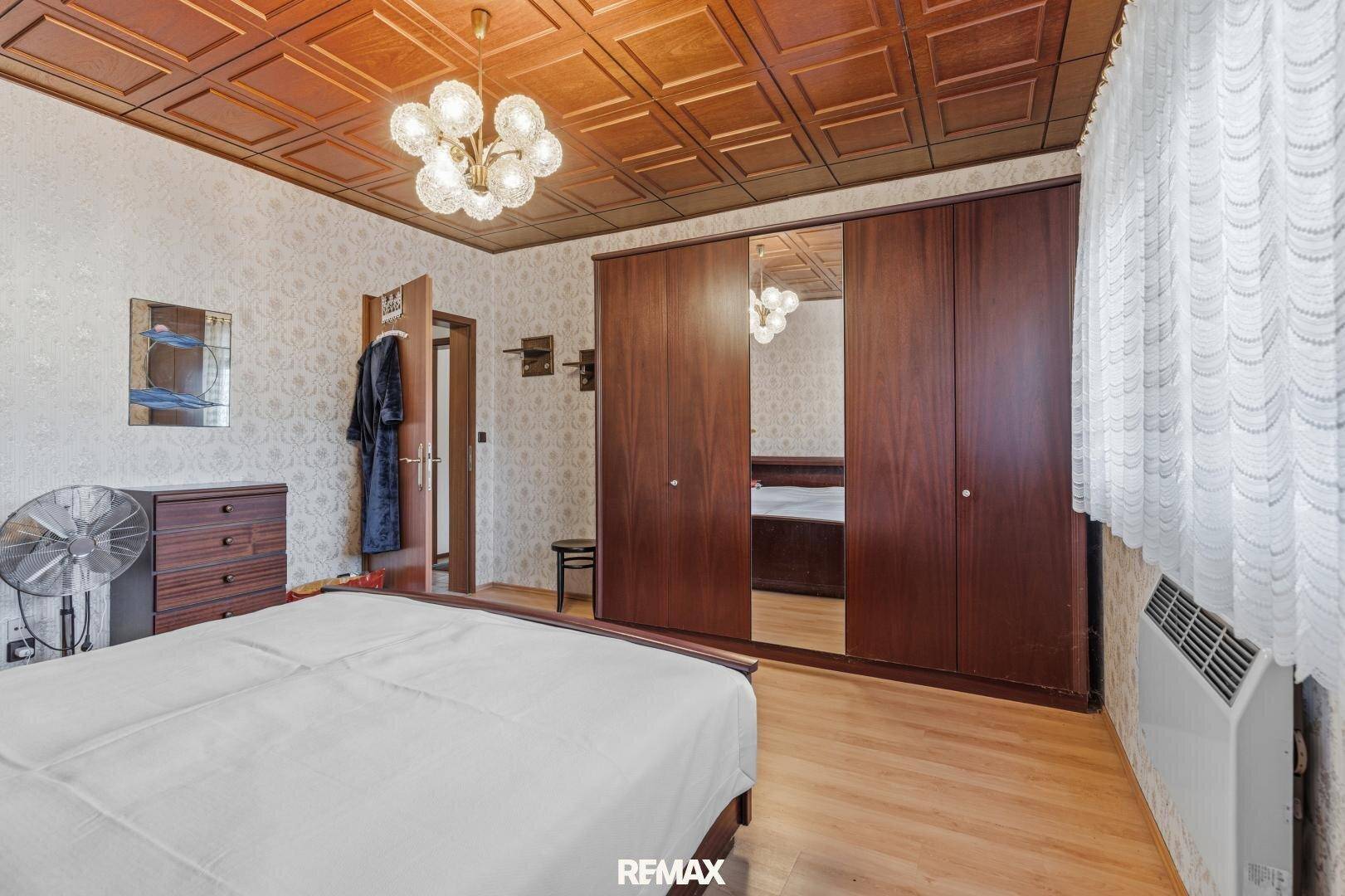 Schlafzimmer mit großem Kleiderschrank, Holzkassettendecke und Parkettboden.