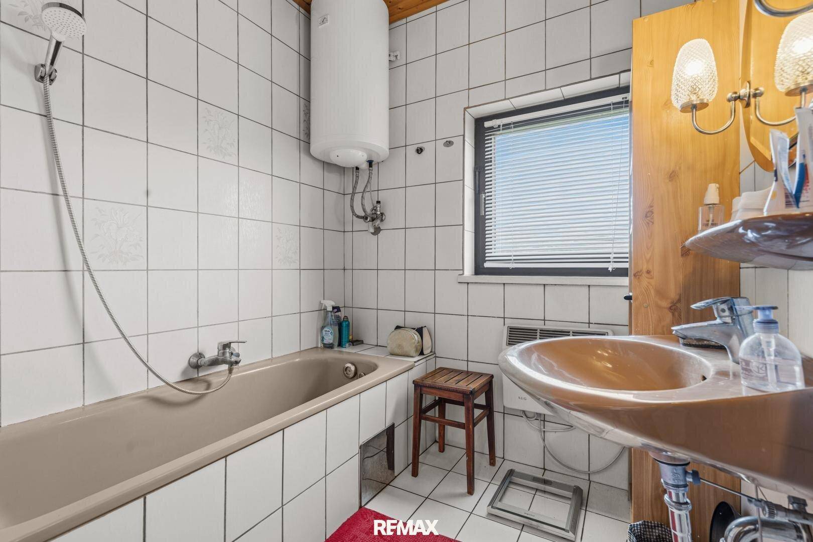 Badezimmer mit Badewanne, Waschbecken und weißen Fliesen, funktional eingerichtet.