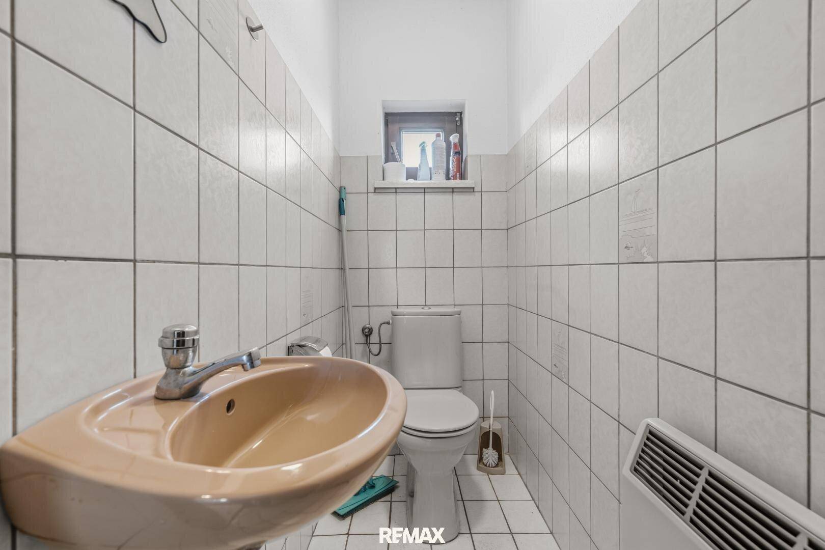 Kleines WC mit Waschbecken, Toilette und weißen Fliesen, hell und sauber.