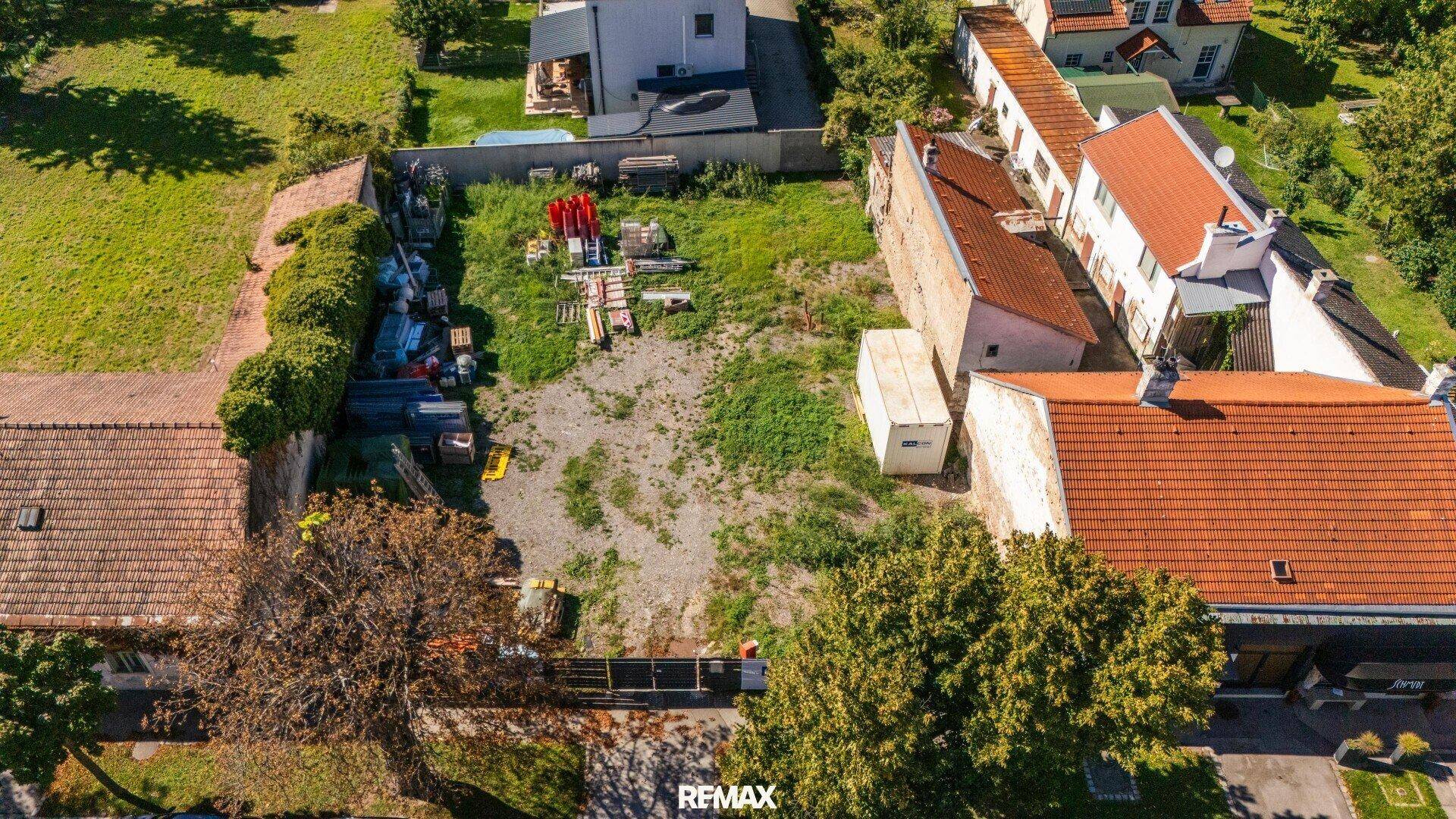 Luftaufnahme eines unbebauten Grundstücks mit angrenzenden Gebäuden und verschiedenen Baumaterialien.