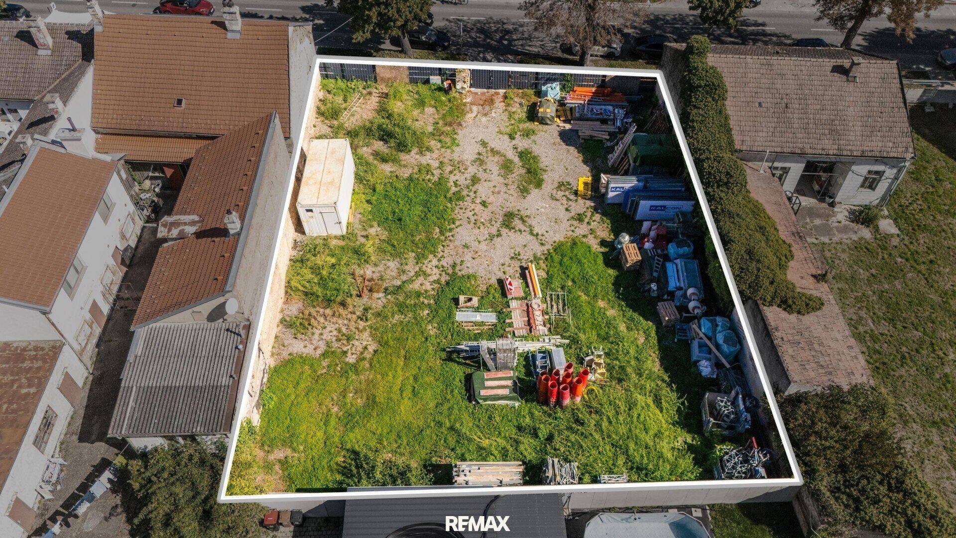 Luftaufnahme eines umrandeten Baugrundstücks mit angrenzenden Häusern und gelagerten Materialien.