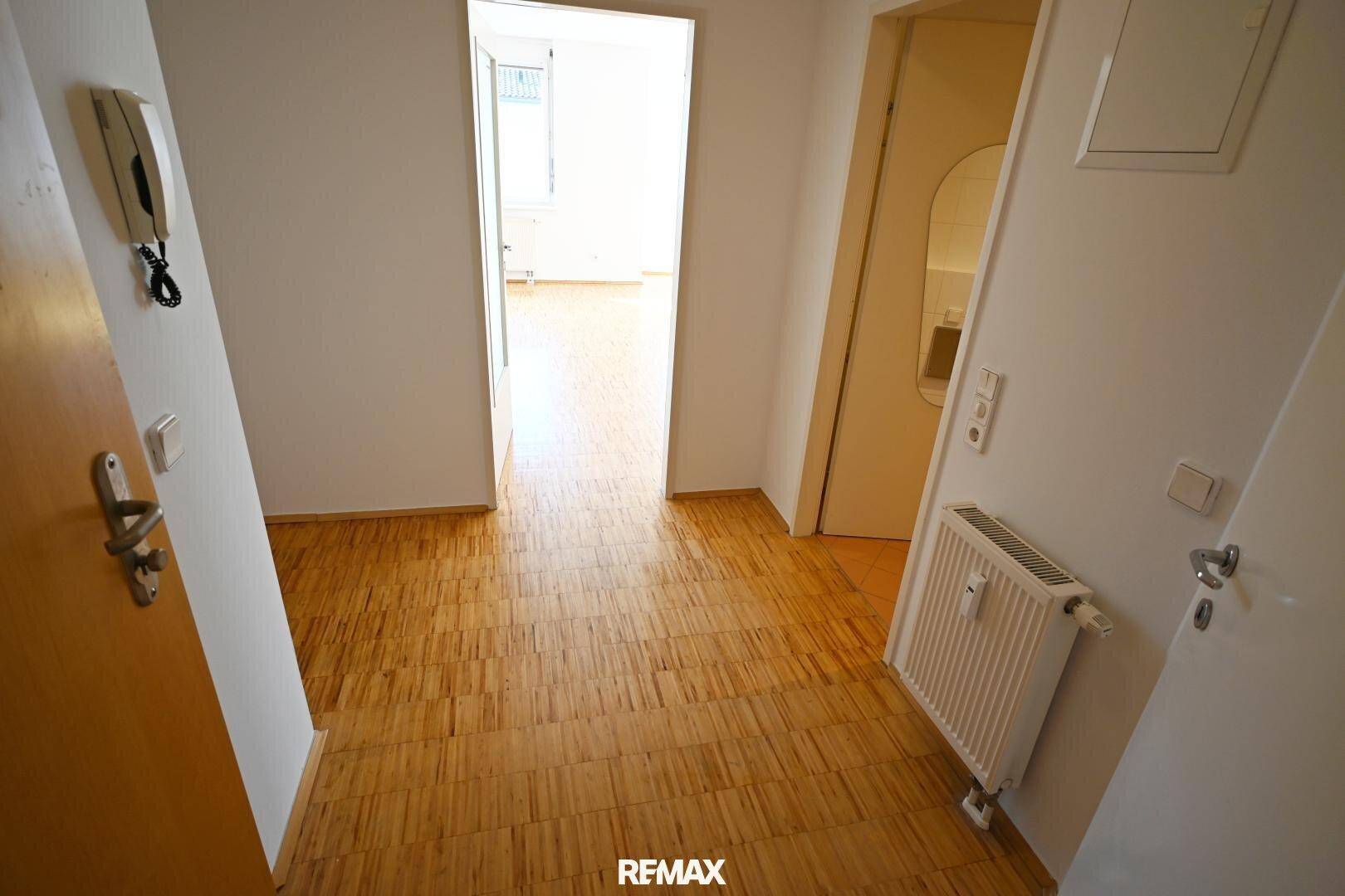 Heller Flur mit Holzfußboden, Gegensprechanlage und Blick in einen weiteren Raum.