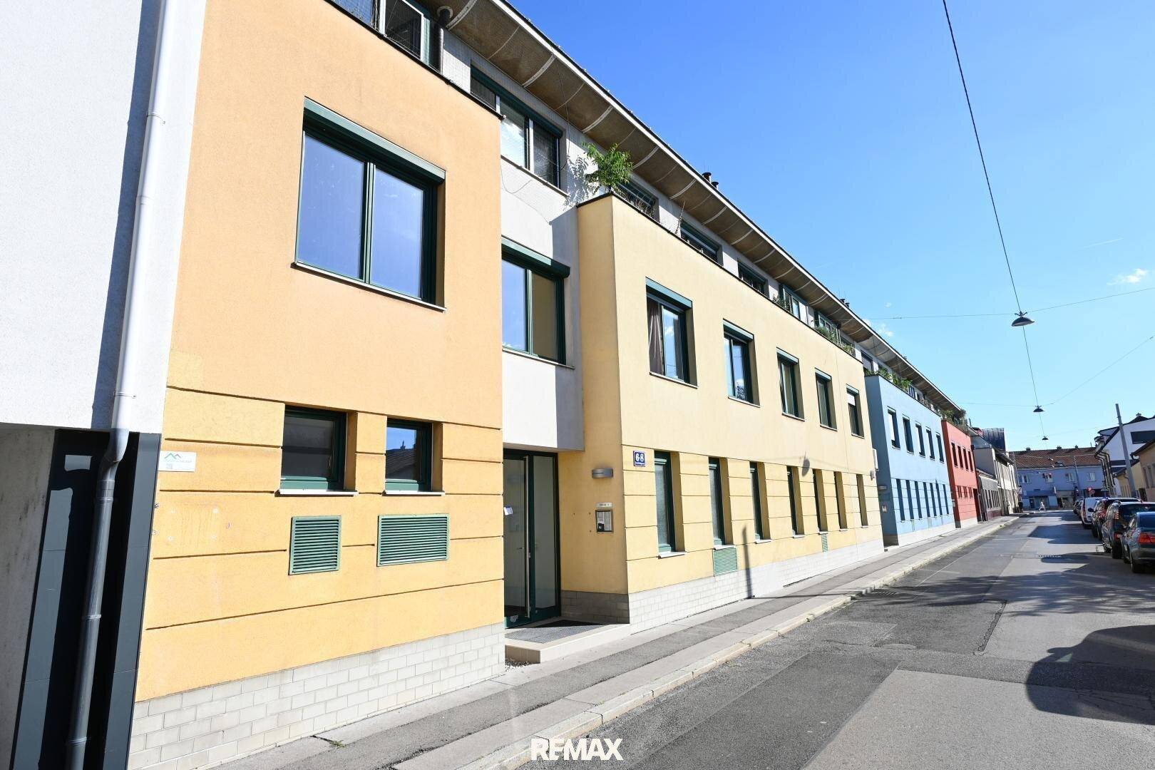 Mehrstöckiges Wohngebäude mit gelber Fassade und grünen Fensterrahmen an einer städtischen Straße.
