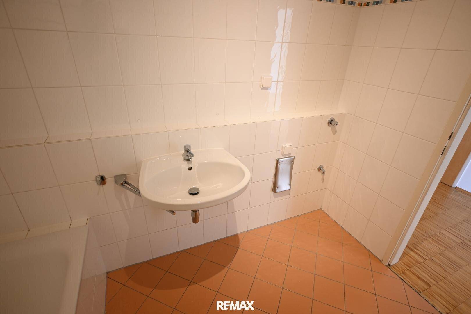 Detailansicht des Waschbeckens im Badezimmer mit weißen Wandfliesen und Terrakotta-Bodenfliesen.