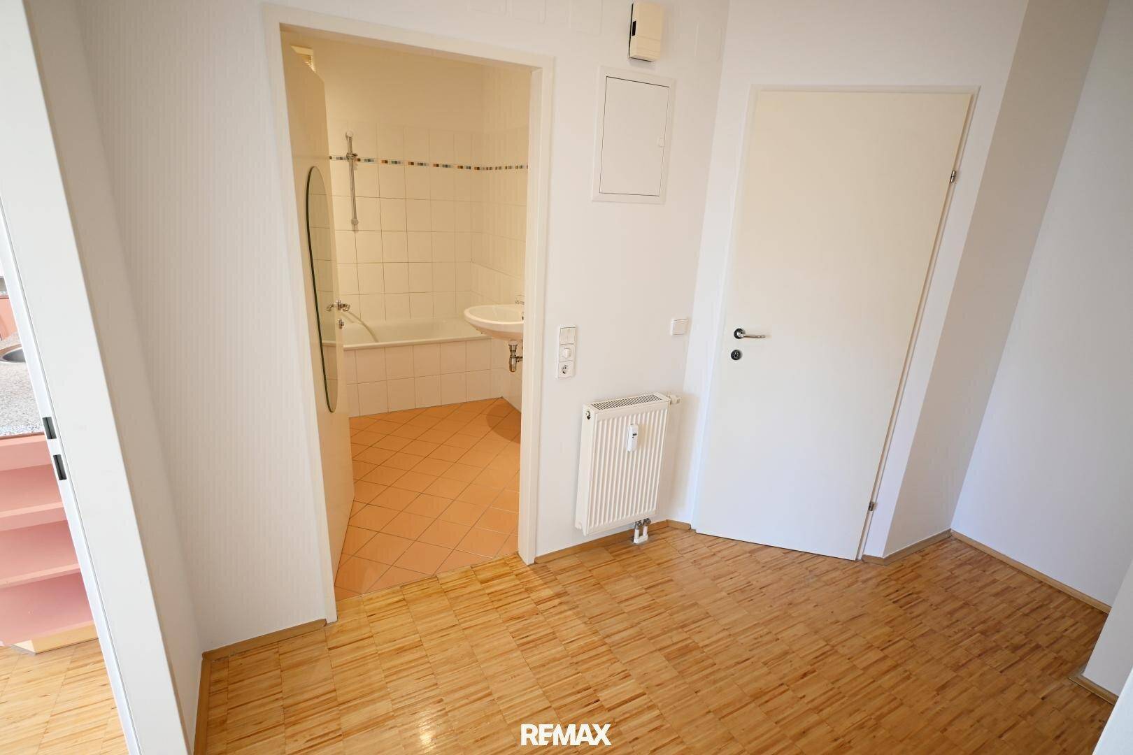 Flur mit Holzfußboden und Zugang zu einem Badezimmer mit Badewanne und Waschbecken.