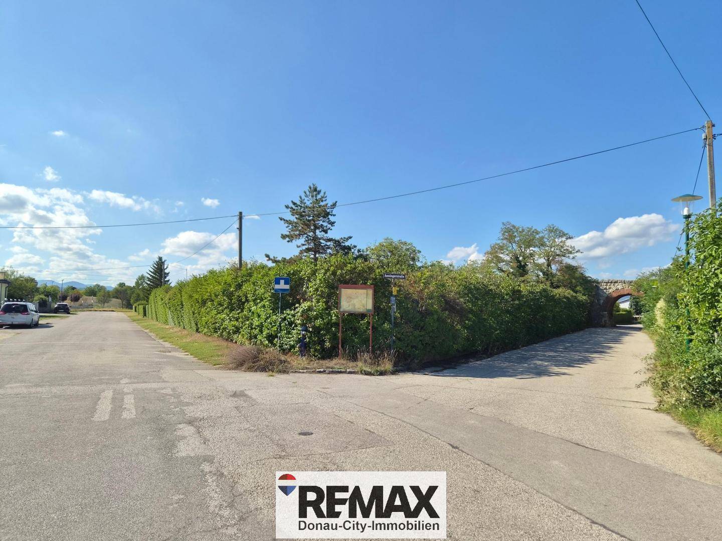 Eine ländliche Straßenkreuzung mit dichten Hecken und Hinweisschildern unter blauem Himmel.