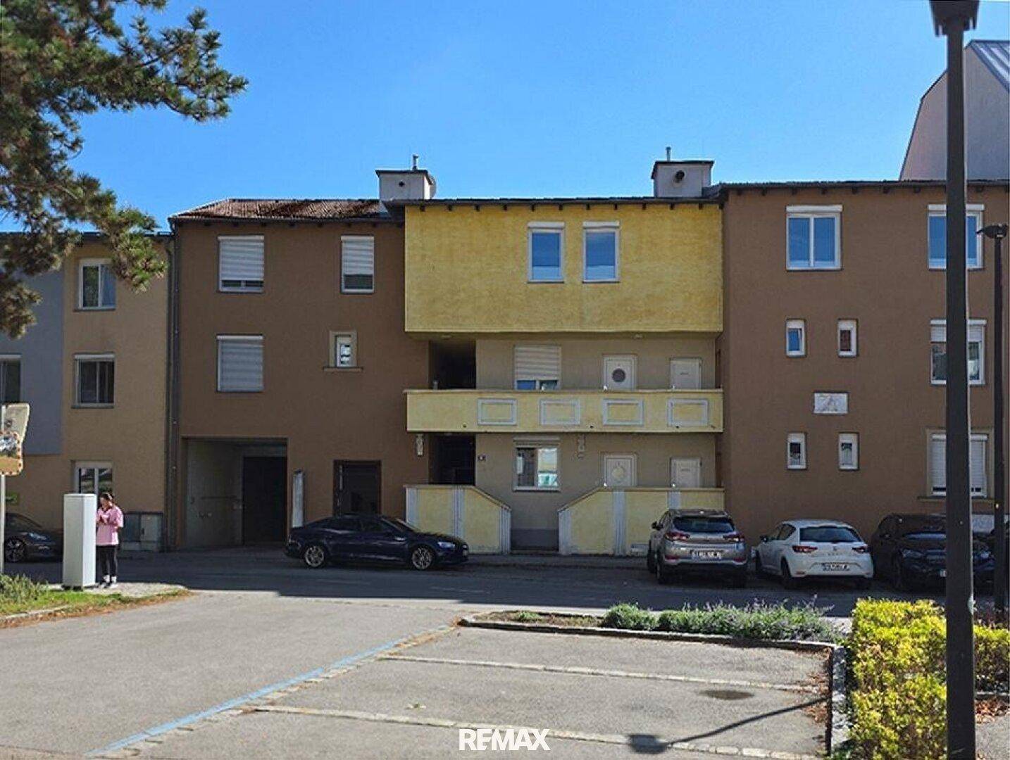 Wohngebäude mit mehreren Etagen, Außenparkplätzen und einer gelben Fassadenakzentuierung.